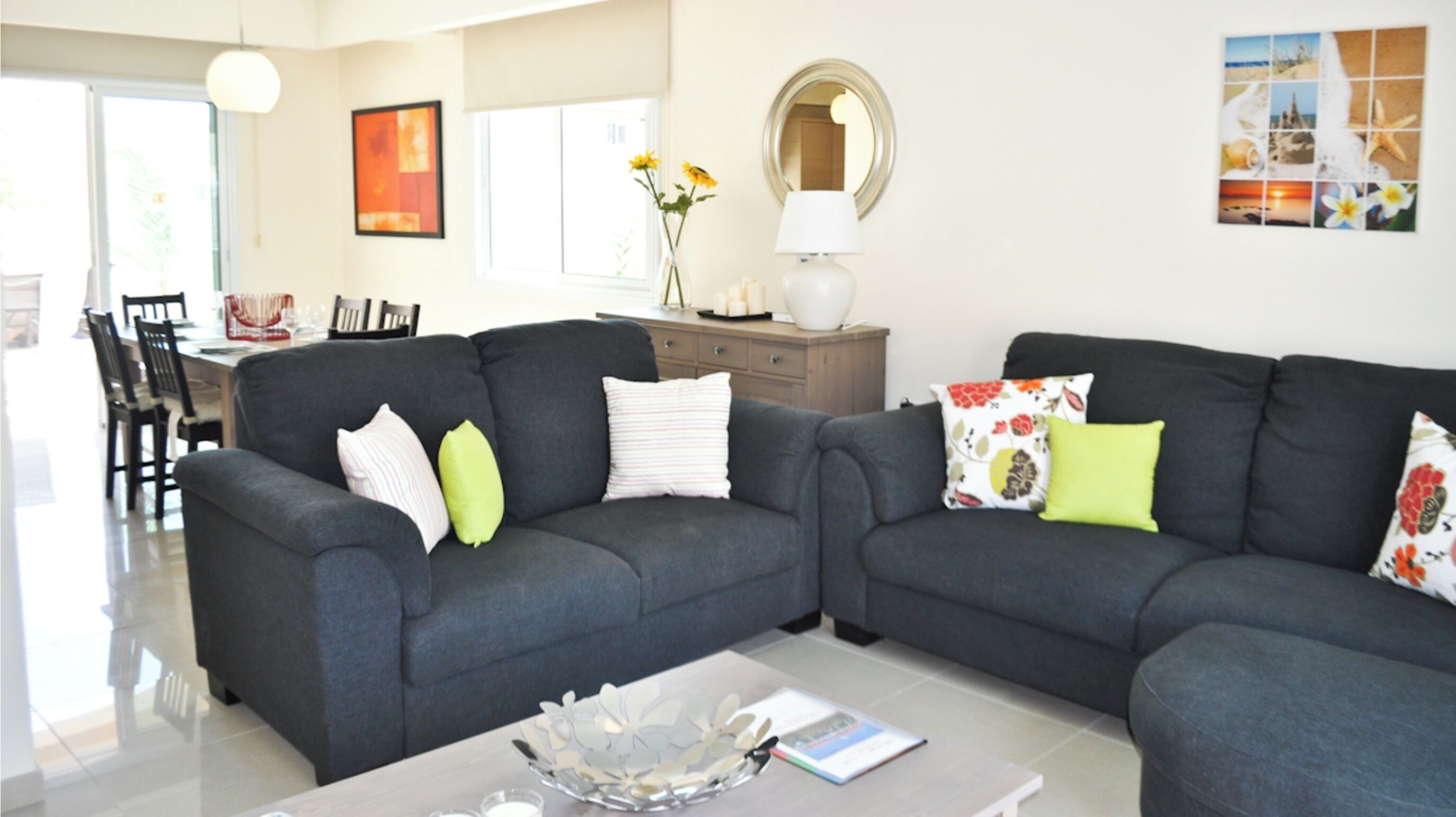 A living room with two dark grey sofas, a coffee table, and a dining area with a table and chairs.
