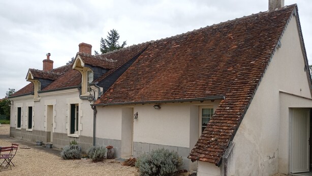 A traditional building with a sloped roof, a chimney, and a gravel driveway.