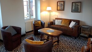A living room with a brown sofa, two armchairs, a wooden coffee table, and patterned floor tiles.