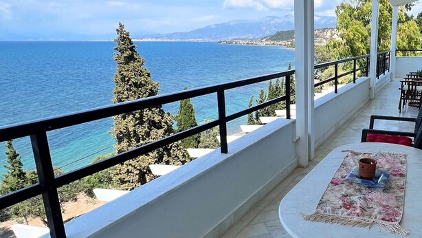 Een balkon met uitzicht op zee, een tafel met vloerkleed en een roze kussen.