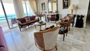 Een ruime woonkamer met een bank, fauteuils en een salontafel. Er is uitzicht op de oceaan door grote ramen.