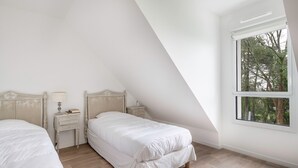 Een slaapkamer met twee bedden, een nachtkastje, een lamp en een raam met uitzicht op bomen.