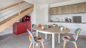 Een moderne keuken met een houten trap, een eettafel met kleurrijke stoelen en een rode kast.