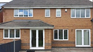 A two-story brick house with a tiled roof, a front porch, and a small garden area. - Stunning 4-bed House in Walsall (Walsall)
