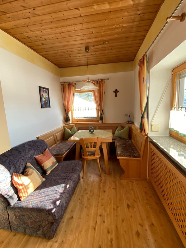 Une pièce chaleureuse avec un plafond en bois, un canapé avec des coussins, une table avec des chaises et une fenêtre avec des rideaux.