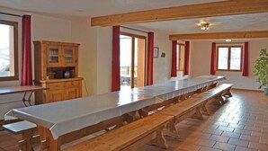 Une longue table à manger avec des bancs, des meubles en bois et des rideaux rouges.