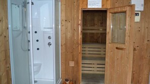 Une cabane en bois dotée d’une douche en verre et d’une porte en bois donnant accès à un sauna.