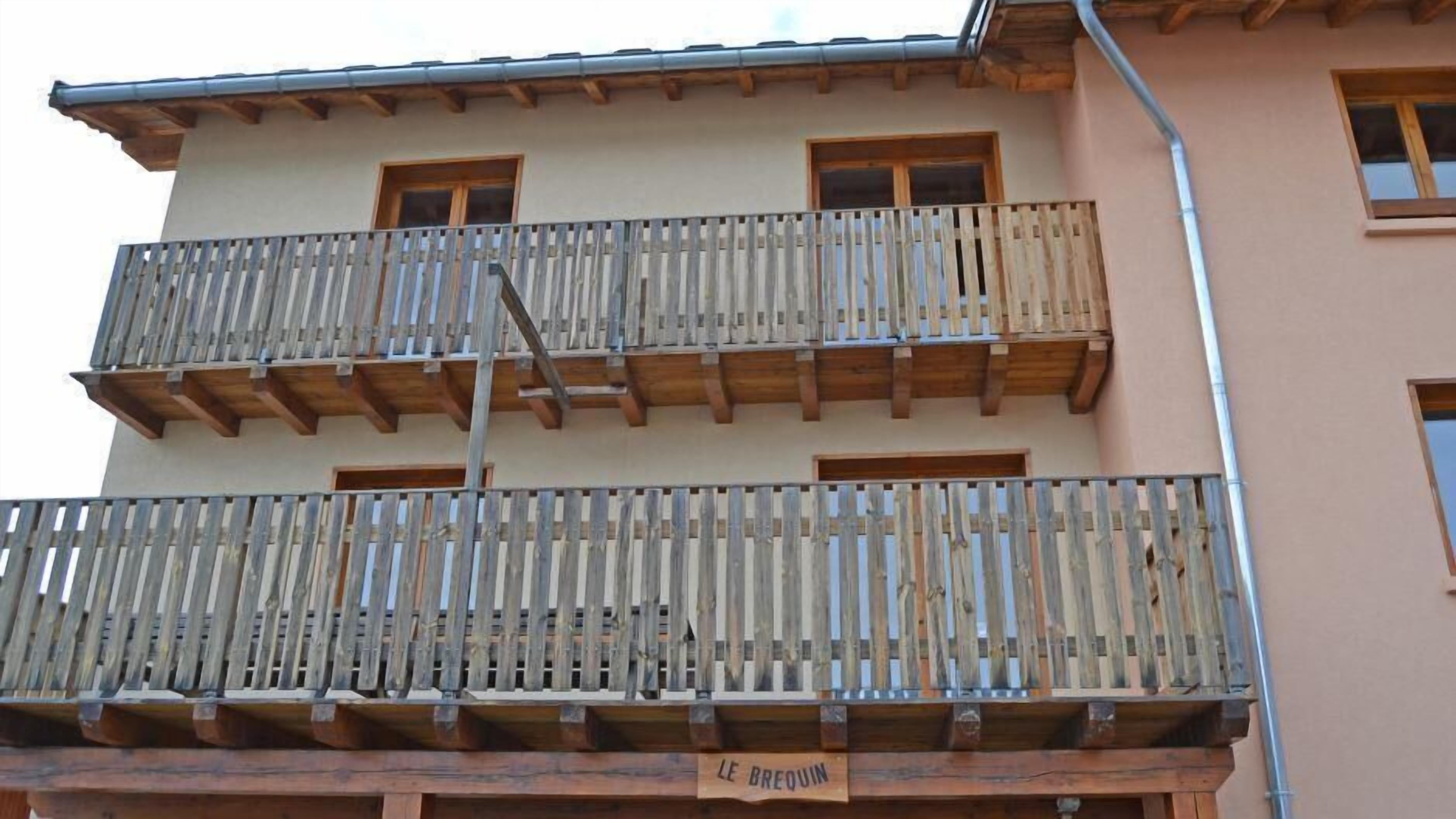 A multi-story building with balconies, wooden railings, and a sign reading "LE BREOUIN".