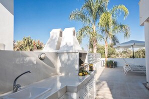 An outdoor kitchen with a built-in grill, a sink, and a seating area with a table and chairs.