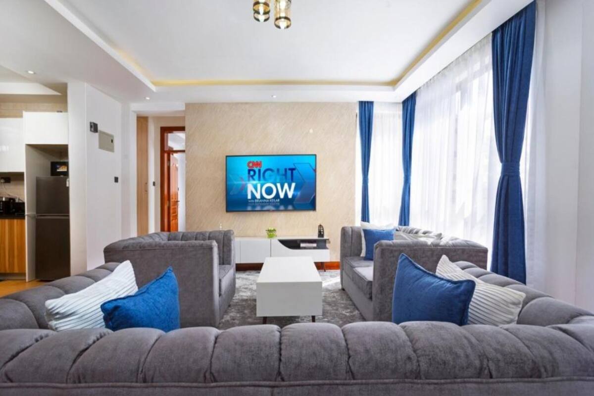 Un saló modern amb un sofà gris, un televisor de pantalla plana muntat a la paret i una taula petita blanca.
