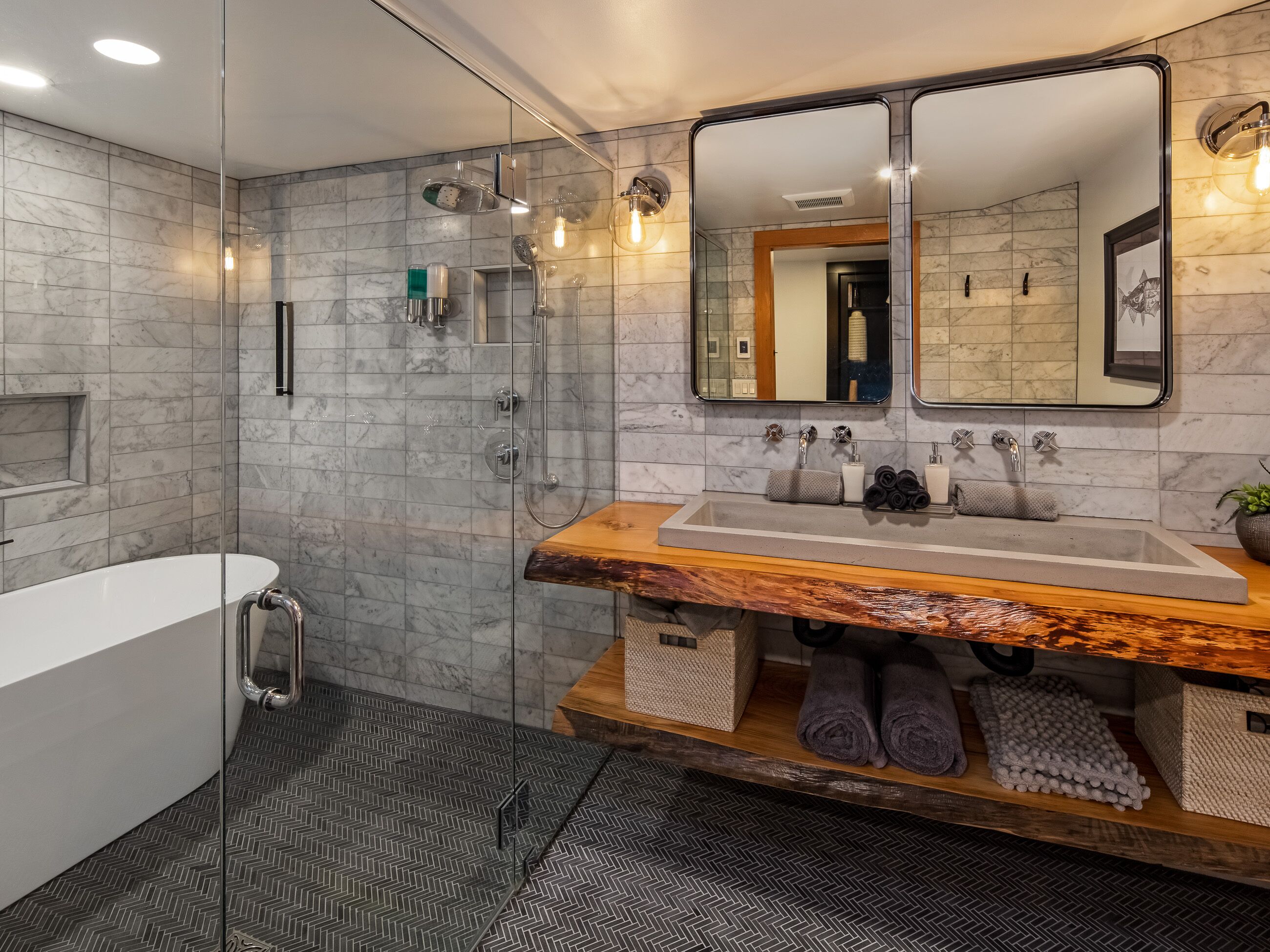 Un baño moderno con ducha envuelta en vidrio, una bañera independiente y un tocador de madera con un espejo grande.