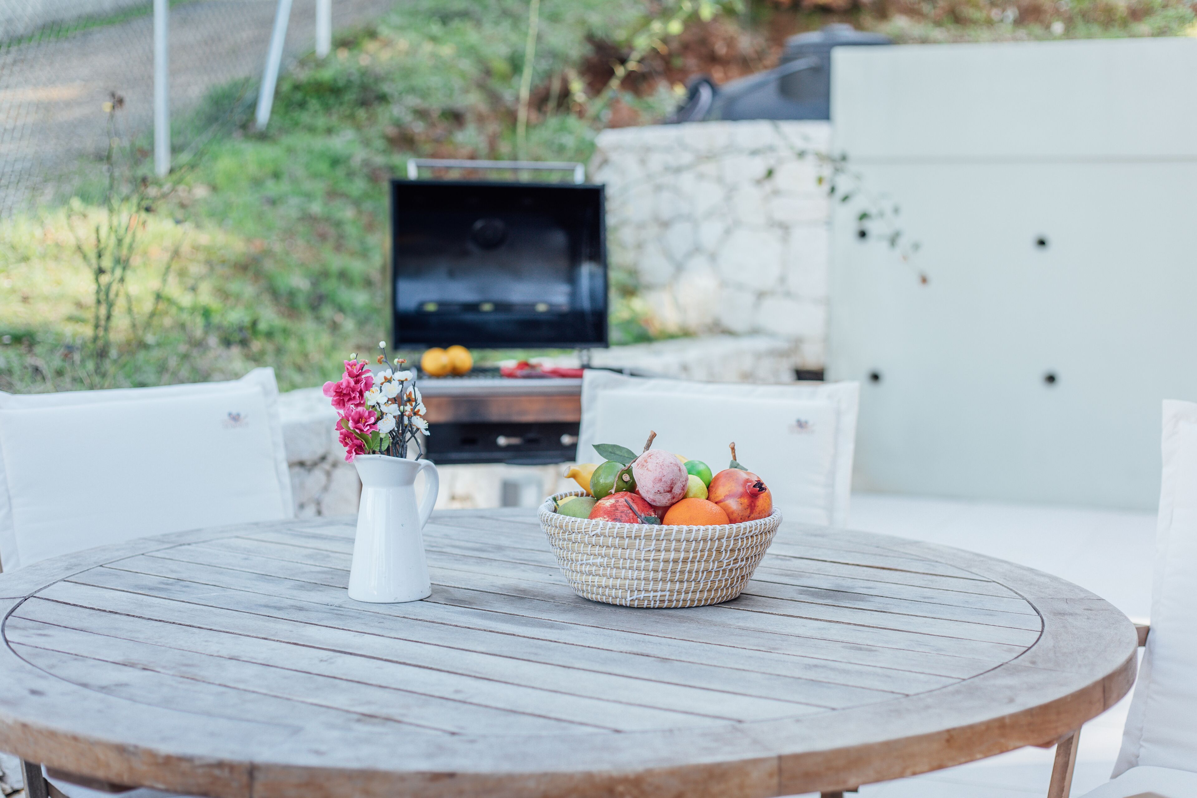 A round wooden table with a white pitcher and a woven basket of fruit.
