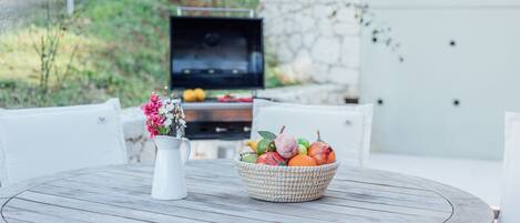A round wooden table with a white pitcher and a woven basket of fruit.