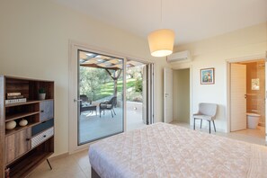 Un dormitorio con una cama grande, un armario de madera, una silla y un ventanal corredero que da a un patio.