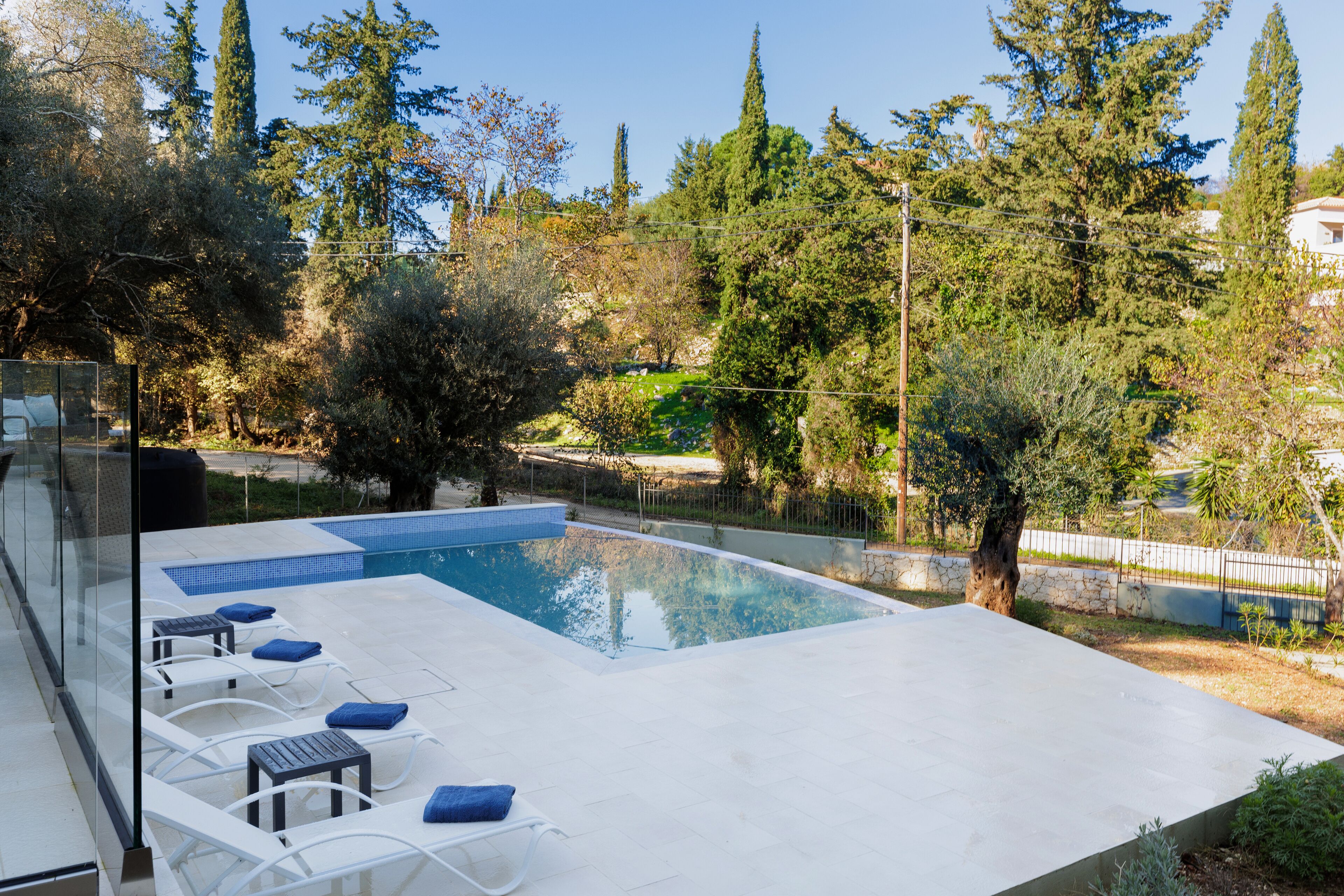 A modern outdoor swimming pool with lounge chairs and a glass balustrade.