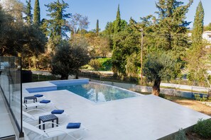 Una piscina moderna al aire libre con tumbonas y barandilla de cristal.
