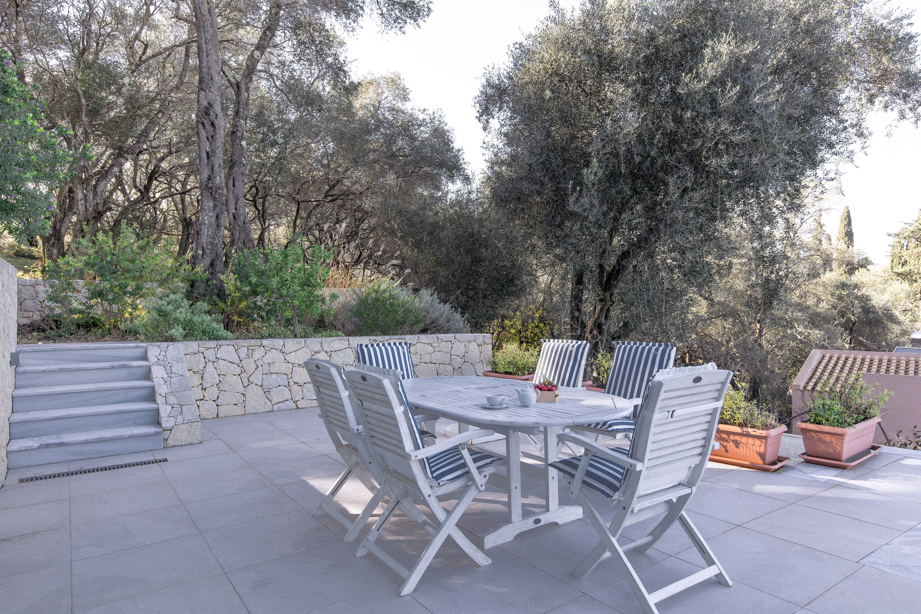 A patio with a stone wall, a table with chairs, and potted plants.