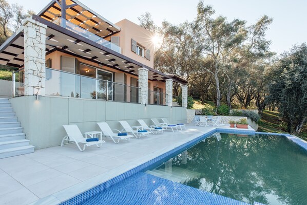 Una casa moderna con piscina, sillones blancos y un pilar de piedra.