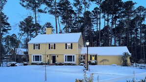 A two-story house with a snow-covered lawn and a white fence in the foreground.
