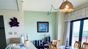 A dining area with a white island, wooden chairs, and a table set with a placemat. - 3 Bedroom Direct Ocean Front Condo in Silver Moon with Outdoor Pool! (Ocean City)