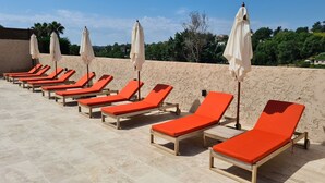 Une rangée de chaises longues, toutes identiques, avec des parasols assortis, sur une terrasse carrelée.