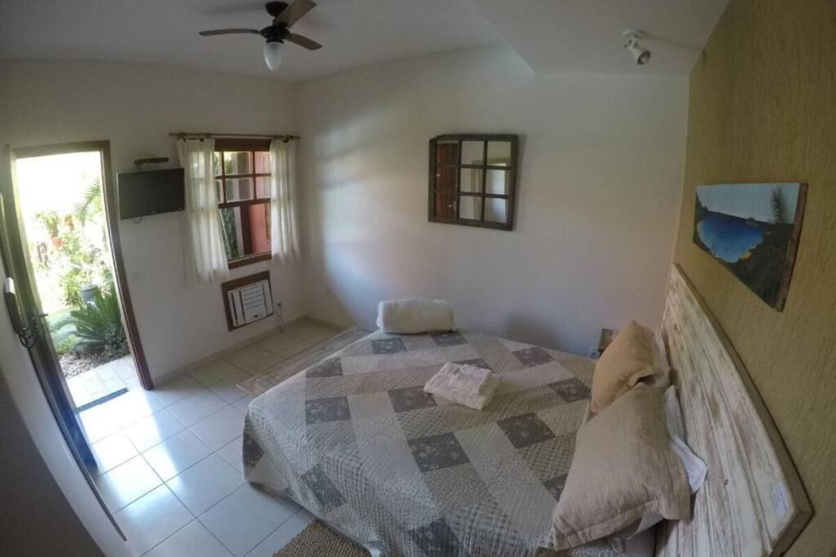 Un dormitorio con cama, ventilador de techo, ventana con cortinas, televisor montado en la pared y un cuadro.
