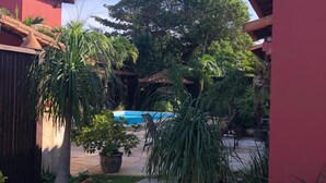 A courtyard with a swimming pool, potted plants, and a red building. - Pousada Casa da Aroeira (Búzios)