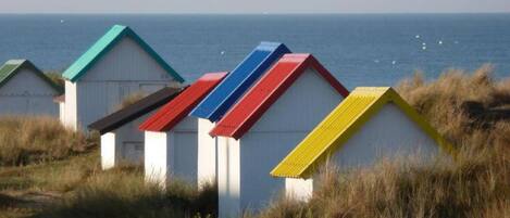 A row of beach huts with colorful roofs, set against a coastal backdrop.