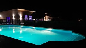 Una piscina de borde curvo, rodeada por una valla y un edificio con ventanas iluminadas.