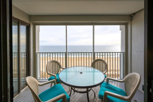 Un balcon avec une table et des chaises en verre, donnant sur une plage.
