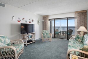 Relax in this stylish living room with a large flat-screen TV, comfortable seating, and a balcony offering ocean views.