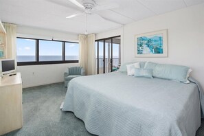 Ett hotellrum med en stor säng, ett skrivbord med en dator, en stol och en balkong med utsikt över havet.