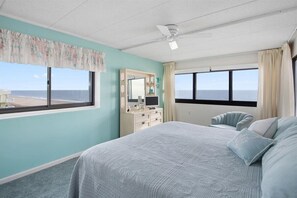 Une chambre avec un lit, une coiffeuse avec un miroir et une vue sur l’océan.