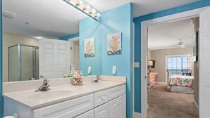 Une salle de bain avec un grand miroir, deux lavabos et un meuble-lavabo avec des tiroirs. On aperçoit une douche au fond.