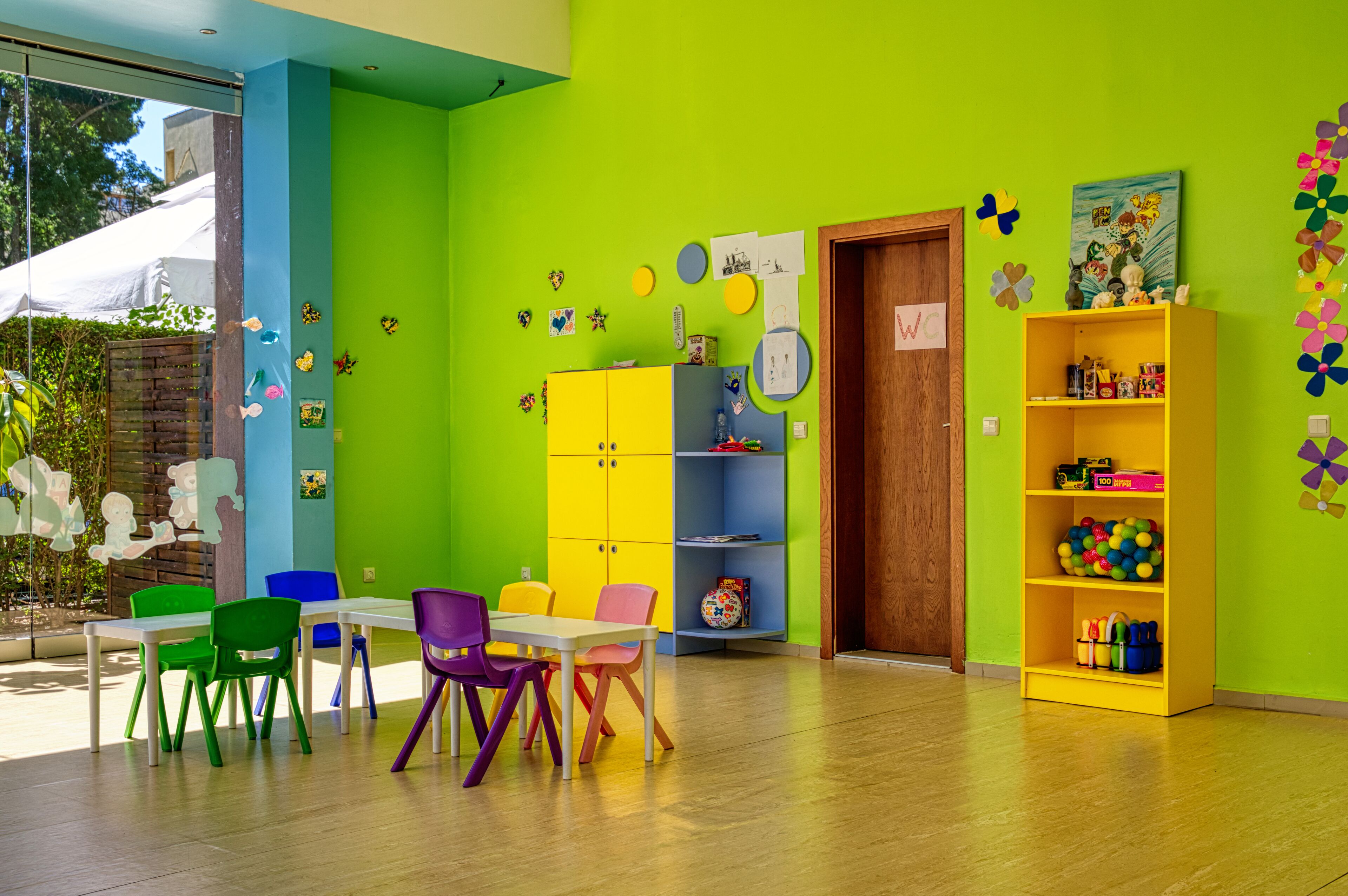 A brightly colored room with a table and chairs, a bookshelf, and a door with a sign.