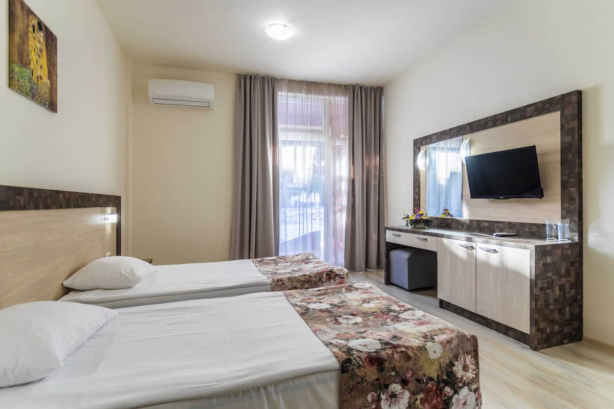 Une chambre d’hôtel avec deux lits, une télévision, un bureau et une fenêtre avec des rideaux.