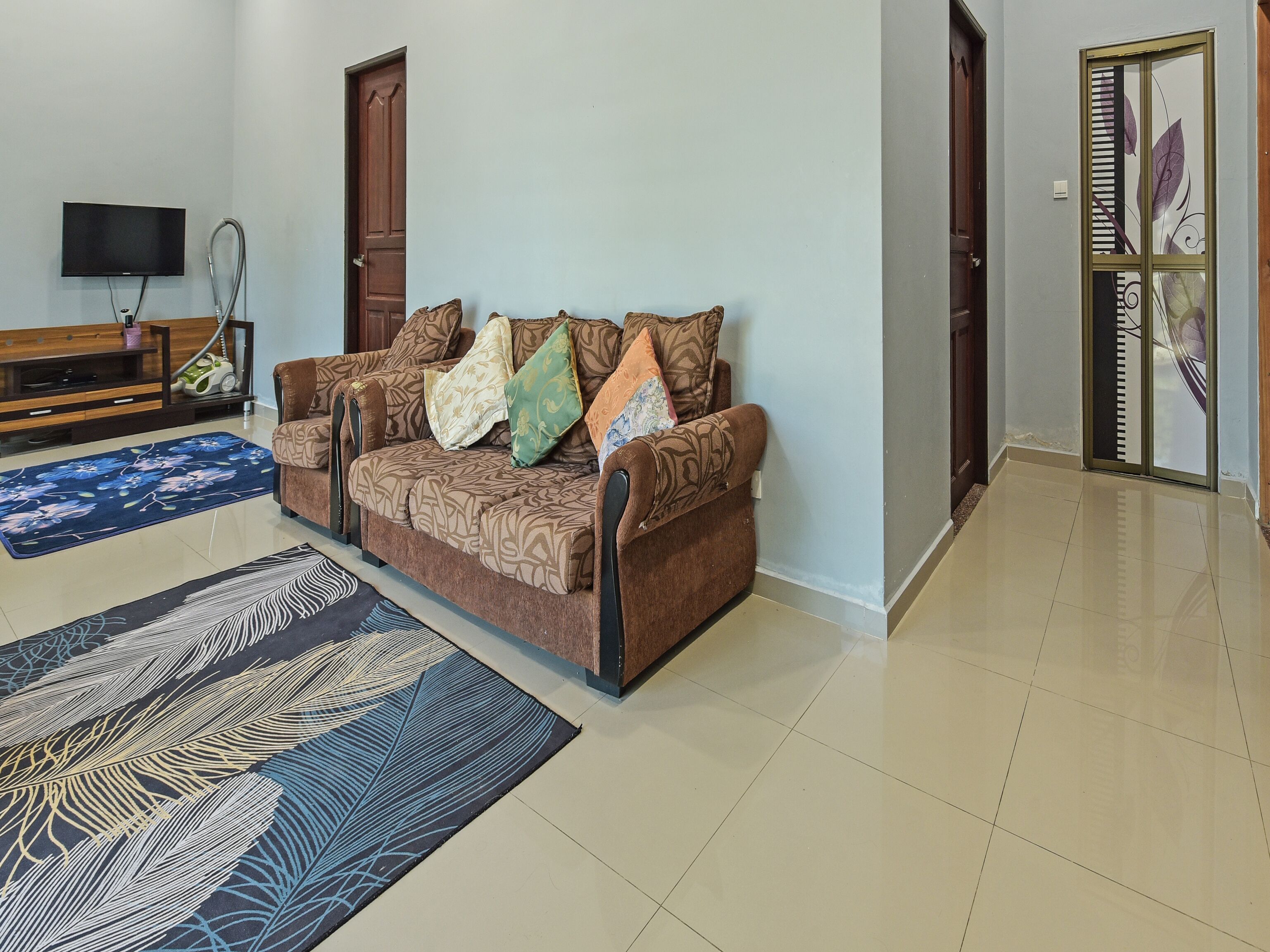 A living room with a sofa, a television, a vacuum cleaner, and a patterned rug.