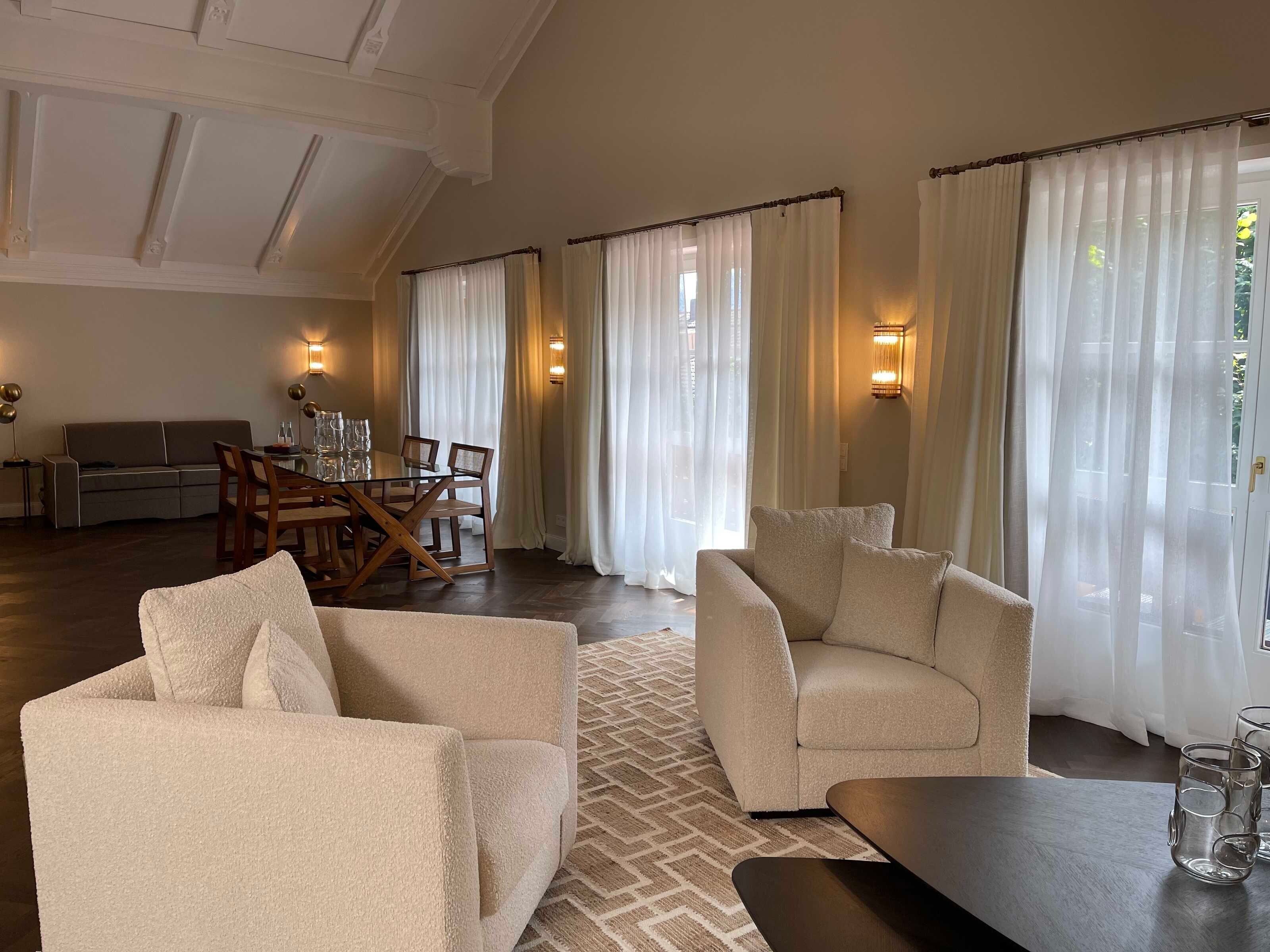 A spacious living room with a high ceiling, a dining area with a wooden table and chairs, and a sofa.