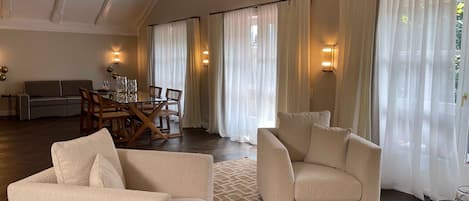 A spacious living room with a high ceiling, a dining area with a wooden table and chairs, and a sofa.