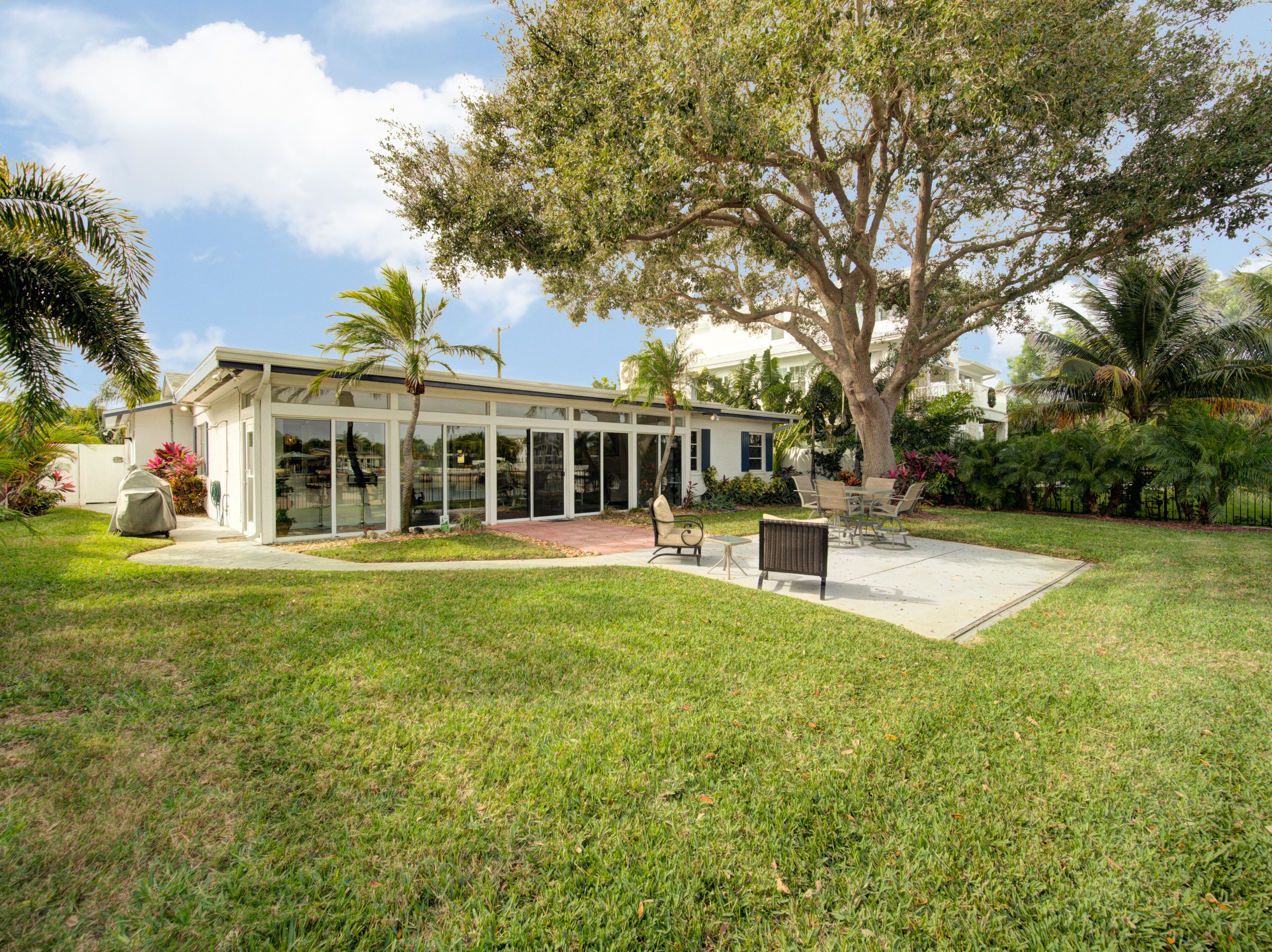 Una casa moderna con un amplio ventanal, un patio con mobiliario exterior y un césped bien cuidado.