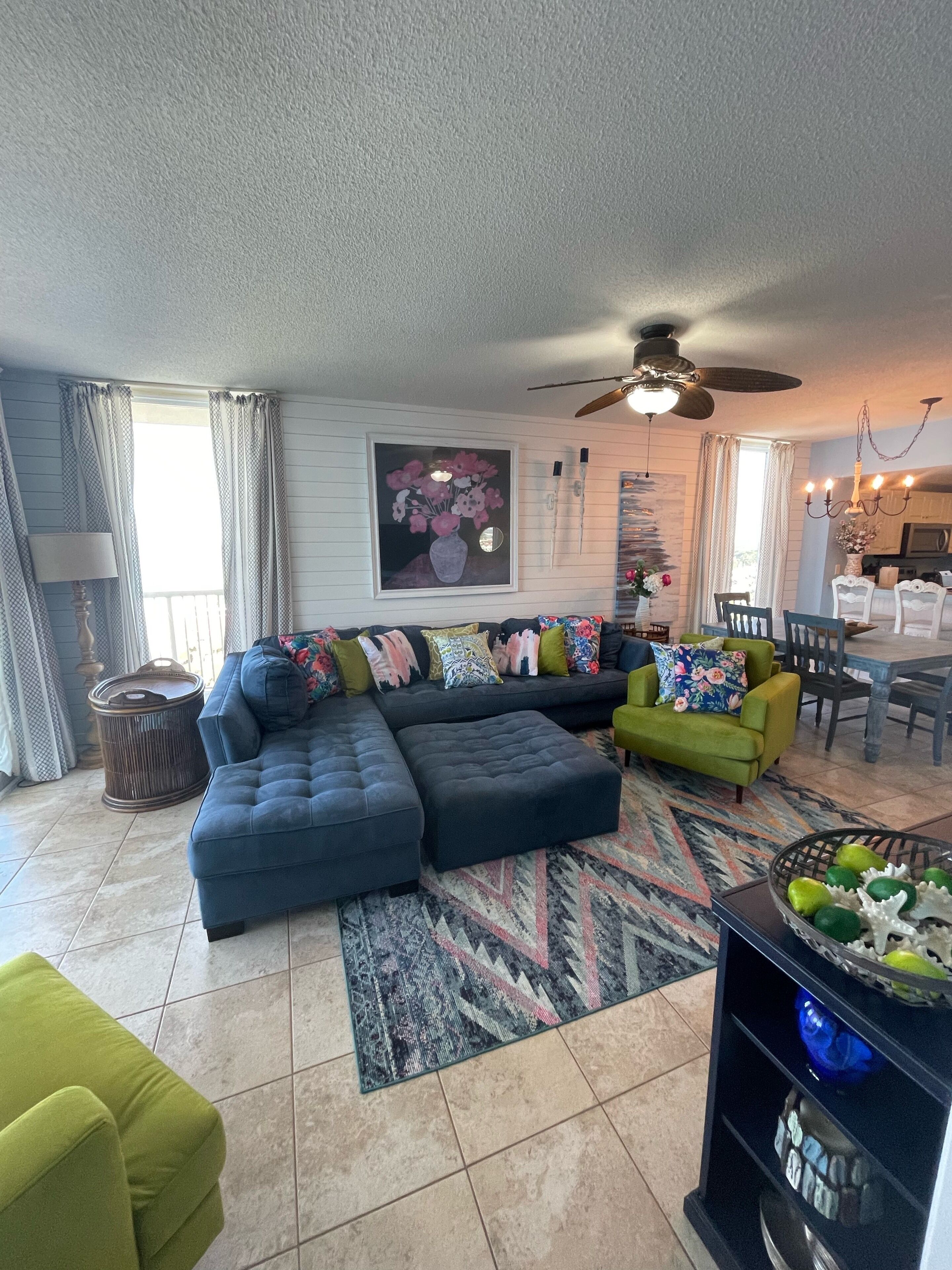 A living room with a sectional sofa, a green armchair, a dining table with chairs, and a ceiling fan.