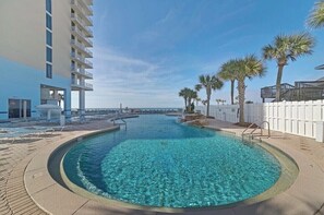 A swimming pool with clear water, surrounded by a white fence, palm trees, and a building with balconies. - BEACH FRONT W/ HUGE BALCONY! FREE WI-FI, 5 POOLS  MAJESTIC BEACH, T-1 FLOOR 13 (Panama City Beach)