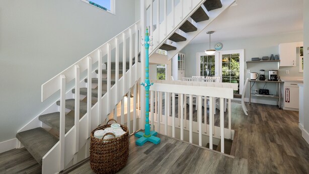 A staircase with white railings and a teal accent pole, leading to a dining area with a white fence and a view of the outdoors. - Island Escape with Pool and Balcony! Near the Beach and Dining - Two Sisters (Holmes Beach)