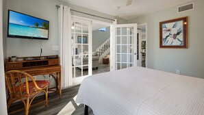 A bedroom with a bed, a television, a wicker chair, and a staircase leading to another room. - Island Escape with Pool and Balcony! Near the Beach and Dining - Two Sisters (Holmes Beach)