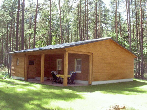 Une cabane en bois avec un porche couvert, deux chaises et une table.