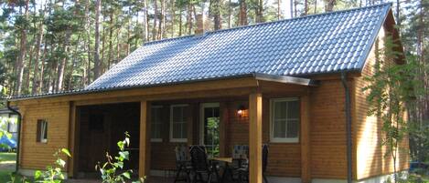 A wooden cabin with a tiled roof, a covered porch, and a small table and chairs.