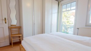 Een slaapkamer met een groot bed, een houten stoel en uitzicht op het omliggende landschap door een raam.