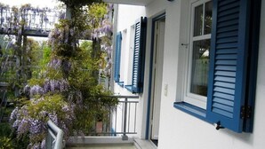 Een balkon met paarse wisteria en blauwe luiken, tegen een witte muur.