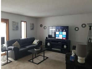 A living room with a dark-colored sofa, a coffee table, a flat-screen TV on a stand, and a lamp. - Spacious 1 BR Apartment located above The Fringe 17 Boutique, Downtown. (Bismarck)