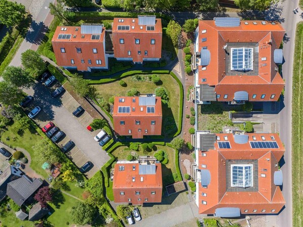 A residential complex with multiple red-roofed buildings, solar panels, and a parking area.